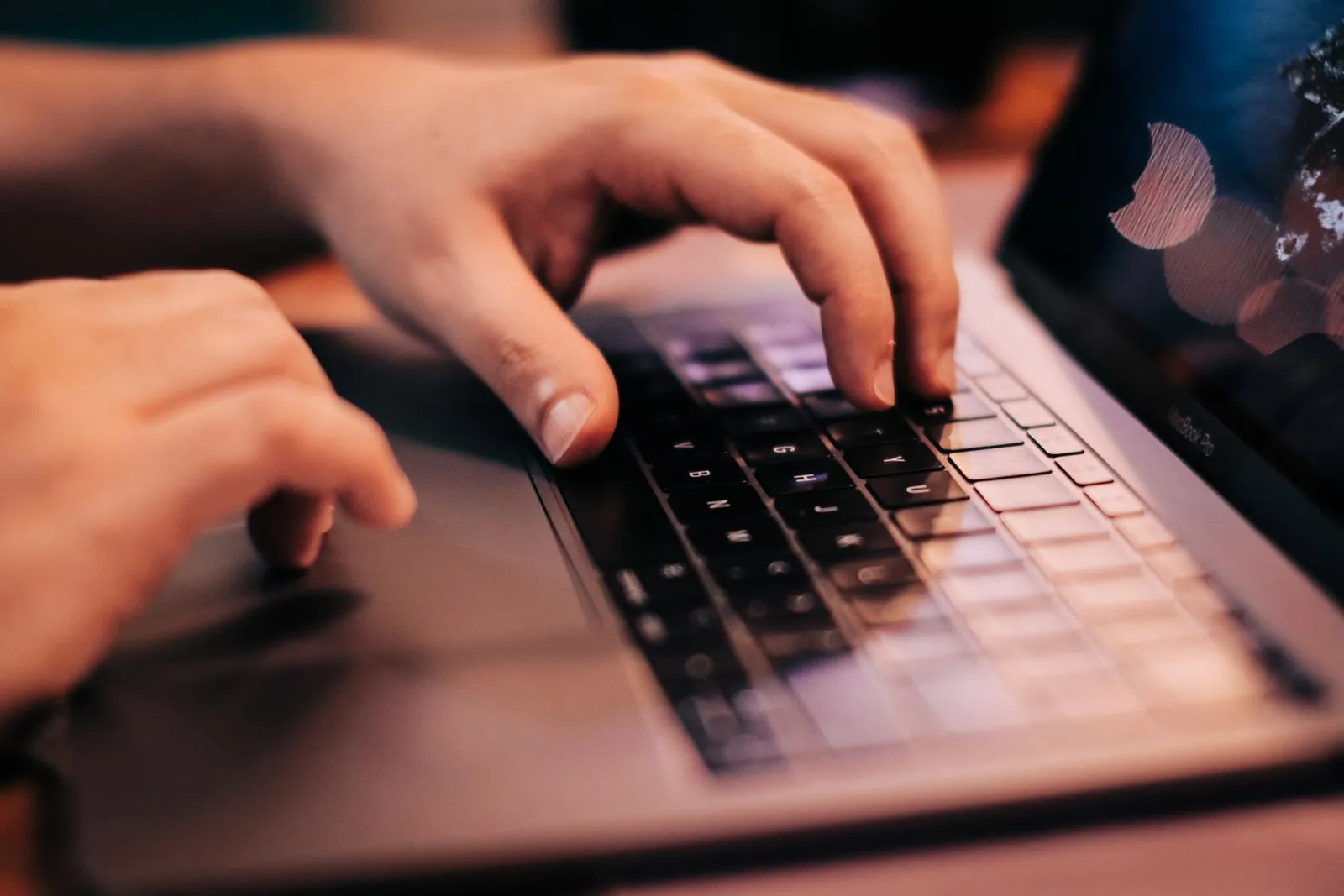 Close-up of hands typing on a laptop keyboard at a desk